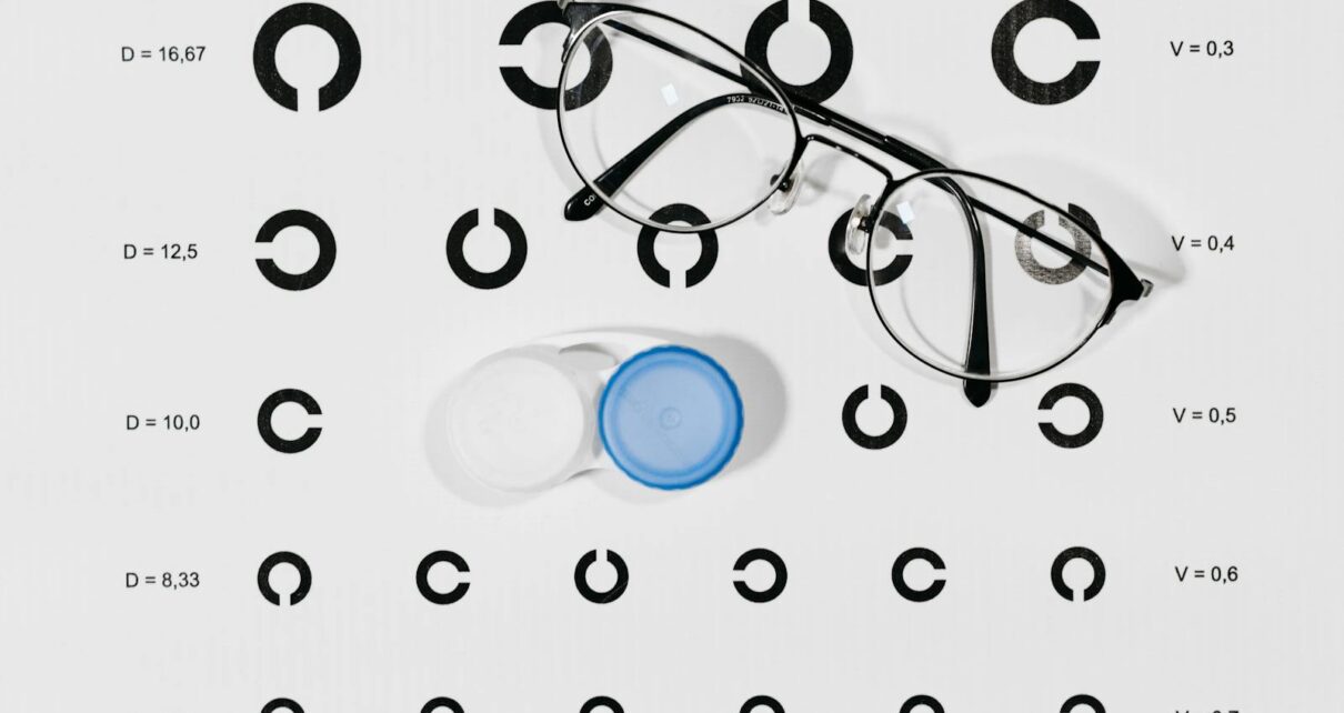 Close-up image of eyeglasses and contact lens case on a Snellen eye chart for vision testing.