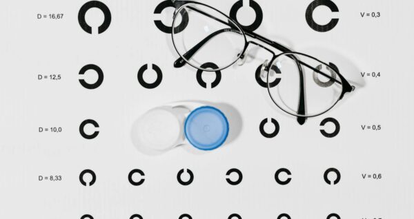 Close-up image of eyeglasses and contact lens case on a Snellen eye chart for vision testing.