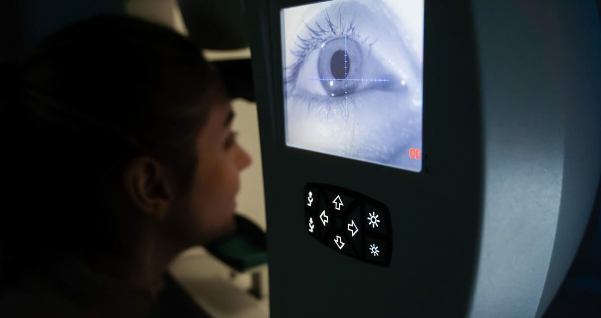 Pacjent z przyciskiem w dłoni siedzi przed computerized perymetrem podczas badania pola widzenia